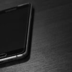 黒いスマートフォンを木目のテーブルに置いたイメージ。楽天モバイルの評判・口コミを紹介する記事のイメージ