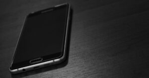 黒いスマートフォンを木目のテーブルに置いたイメージ。楽天モバイルの評判・口コミを紹介する記事のイメージ