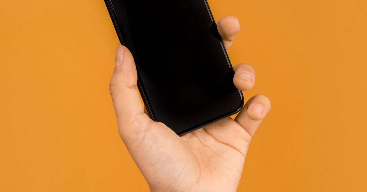 オレンジ色の背景の前でスマートフォンを手に持っている