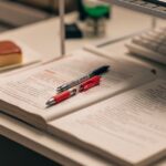 開いた本とノート、ペン、ノートパソコンが並ぶ学習机