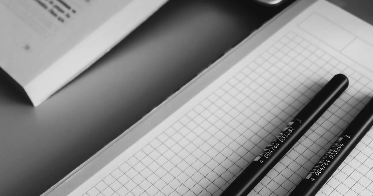 白黒で撮影された勉強机のクローズアップ。ノートとペン