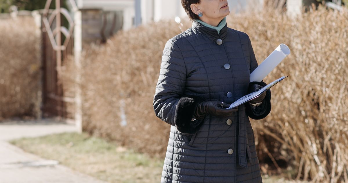 書類を手にした作業服の人が住宅の外まわりを確認している
