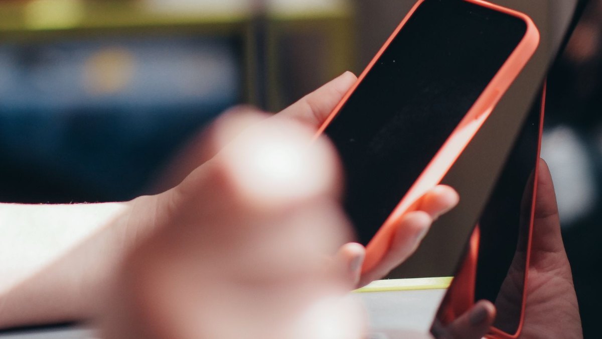 ノートパソコンの横でスマートフォンを操作する手元